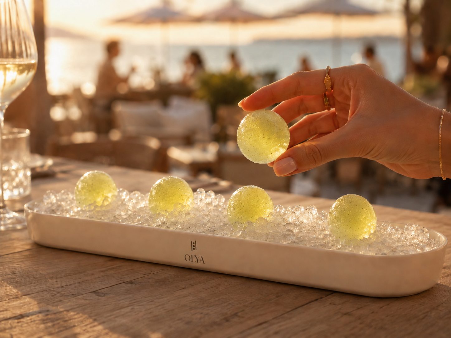 Une main cueille une perle OLYA sur la glace pilée, en beach club de jour